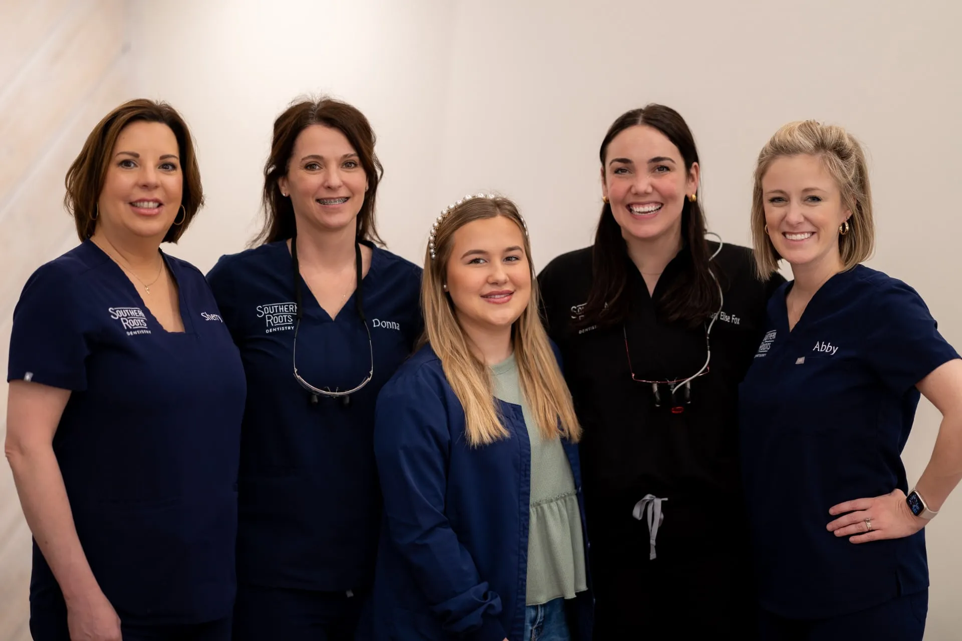 Group of dental professionals from Southern Roots Dentistry, featuring Lindsey and team members in navy scrubs, smiling in a bright clinic setting.